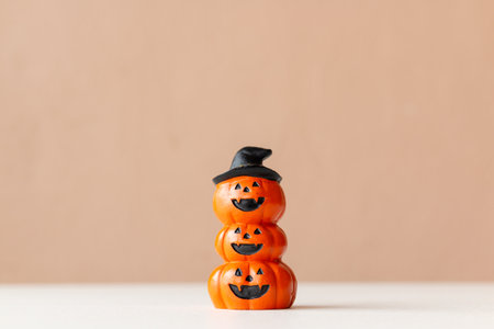 Stacked Halloween pumpkin figurine with carved faces and a witch hat on top on neutral background.の写真素材