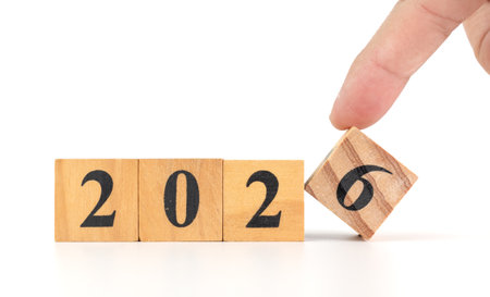 A hand flips a wooden block to change the year from 2025 to 2026, symbolizing New Year, future...