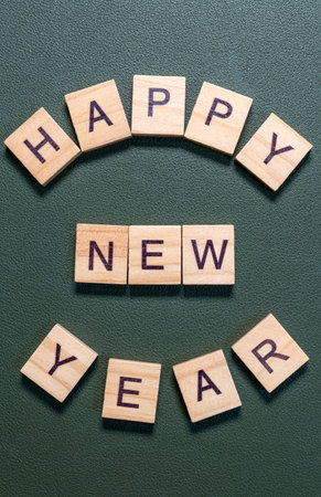 Wooden letter tiles spelling Happy New Year arranged neatly on a textured green background, minimal...