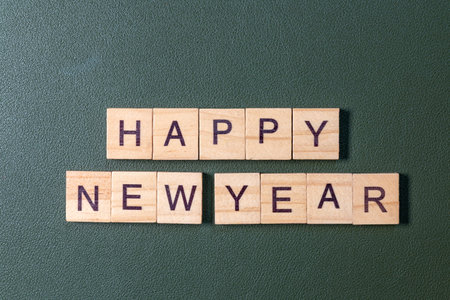 Wooden letter tiles spelling Happy New Year arranged neatly on a textured green background, minimal...