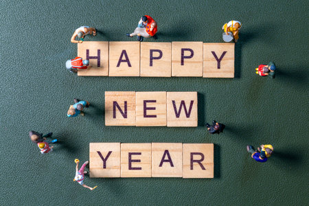 Creative flat lay of miniature figurines surrounding wooden letter tiles forming the phrase Happy New Year on a green textured backgroundの写真素材