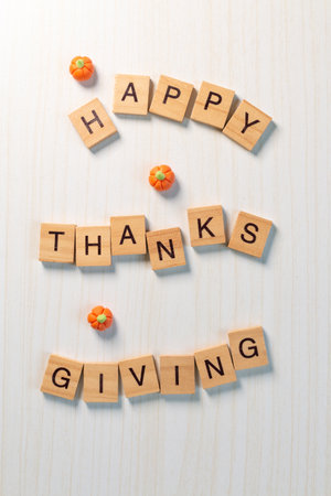 Top view of wooden letter Happy Thanksgiving with mini pumpkins on light wood background, festive minimal holiday concept.の写真素材