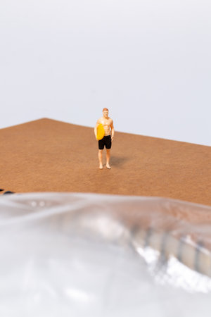 Tiny surfer figure stands on a notebook beside a sheet of plastic, symbolizing environmental issues, pollution, and ocean awareness in a creative concept scene.の写真素材