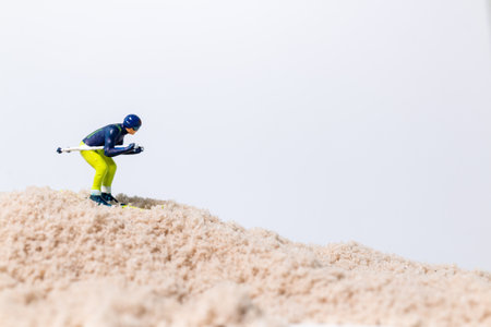 Miniature skier figure skiing on sand surface with white background, creative sport concept with copy space.の写真素材