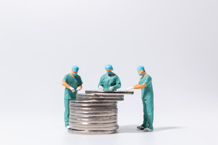 Miniature doctors examining a stack of coins on white background, healthcare finance and medical cost concept with teamwork and planning.の写真素材