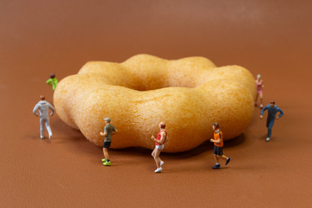 Miniature runners jogging around a donut, representing calorie burning, fitness motivation, and the balance between exercise and sweet food consumption.の写真素材