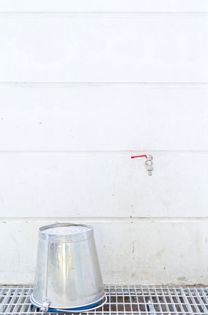 Old tap and bucket on white wallの写真素材