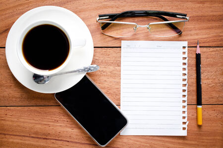 empty notebook and a cup of coffee on the wooden desk backgroundの写真素材