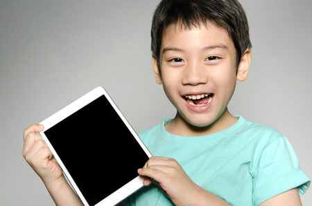 Little asian boy smiles with tablet computer on gray backgroundの写真素材