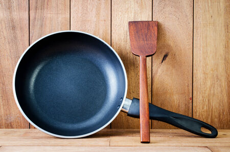 Closeup of  iron frying pan and wooden utensils on wood wall background . の写真素材