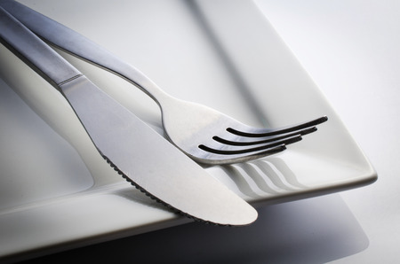 Used Cutlery set with Fork, Knife on white dish, isolated on gray background . 