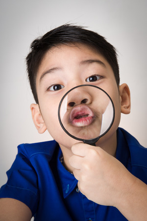 portrait of a young asian child looking through a magnifying glass on gray backgroundの写真素材