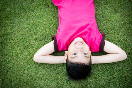 Little Asian child laying down on the grassの写真素材