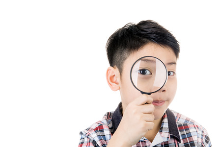 portrait of a young asian child looking through a magnifying glass on white backgroundの写真素材