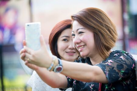 Happy asian woman whith friend taking a selfie - Best female friends catching the moment with modern smartphoneの写真素材