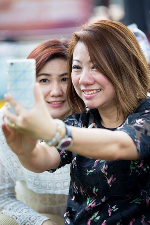 Happy asian woman whith friend taking a selfie - Best female friends catching the moment with modern smartphoneの写真素材