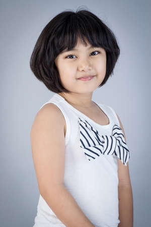 Happy asian child in white dress on gray backgroundの写真素材