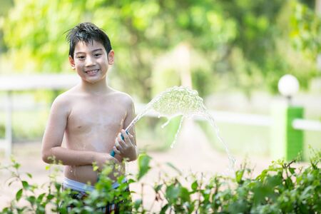 Little Asian boy watering the tree, standing in the shade of a tree in the garden on a hot summer day.の写真素材