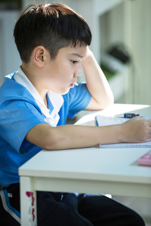 Young asian boy doing his homework and thinkingの写真素材
