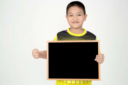 Little asian boy holding empty wood blackboard in sport uniform on gray backgroundの写真素材