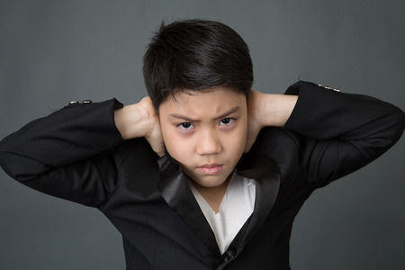 Little asian boy in black suit upset, depression face on gray backgroundの写真素材
