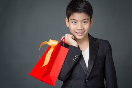 Portrait of asian boy in black suit holding gift bagon gray backgroundの写真素材