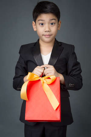 Portrait of asian boy in black suit holding gift bagon gray backgroundの写真素材