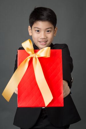 Portrait of asian boy in black suit holding gift bag on gray backgroundの写真素材