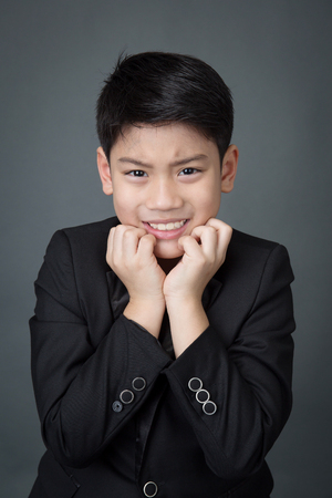 Little asian boy in black suit upset, depression face on gray backgroundの写真素材