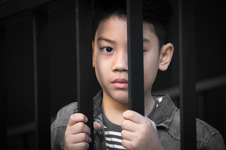 asian boy Hand in jail looking out the windowの写真素材