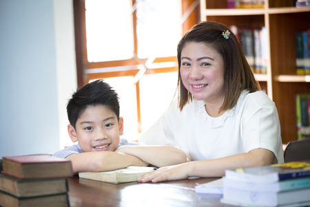 Portrait of happy boy and teacher reading book by bookshelf in libraryの写真素材