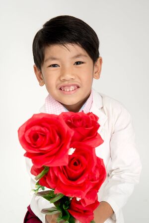 Little Asian boy in vintage suit with red rose in hand. Over gray background with smile faceの写真素材