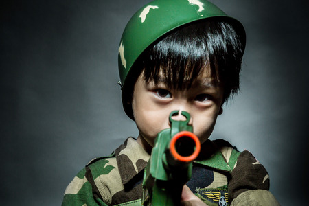 Young asian boy dressed like a soldier with rifle on gray backgroundの写真素材