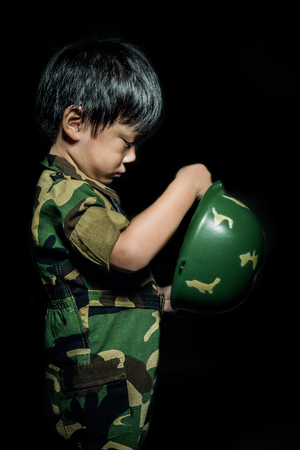 Young asian boy dressed like a soldier with rifle on gray backgroundの写真素材
