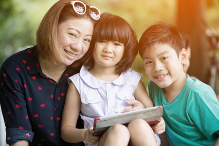 Asian family are playing together with a computer tablet in the park, Bangkok Thailandの写真素材