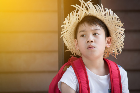 Asian bored child with red backpack is thinking while with sun lightの写真素材