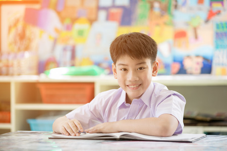 Happy asian child reading book and looking camera ,with sunlight in morningの写真素材