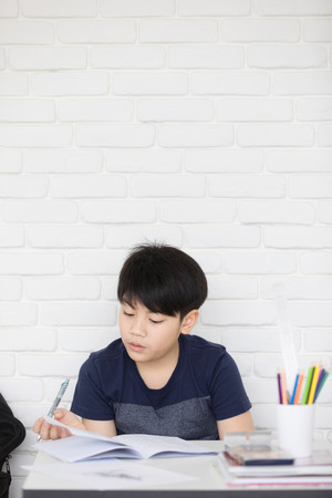 Happy Asian boy doing homework near white brick wallの写真素材