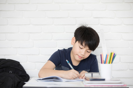 Happy Asian boy doing homework near white brick wallの写真素材