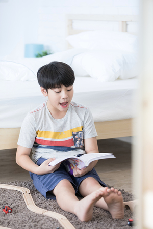 Asian boy sit on the floor and reading book with smile face at home.の写真素材