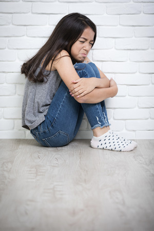Depressed young asian girl sitting on floor at homeの写真素材