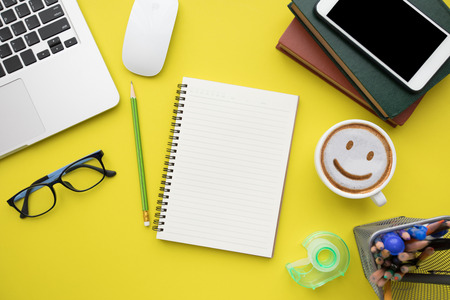 Modern yellow office desk table with laptop and blank notebook page for input the text. Top view,...