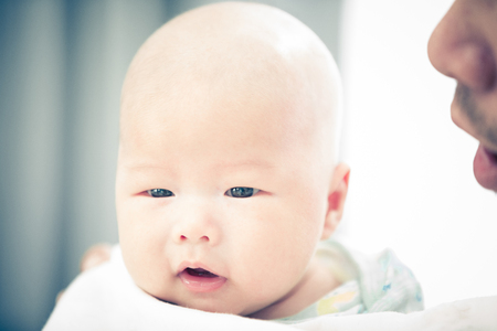 Asian father and baby son plays, hugging, playing at home on bedの写真素材