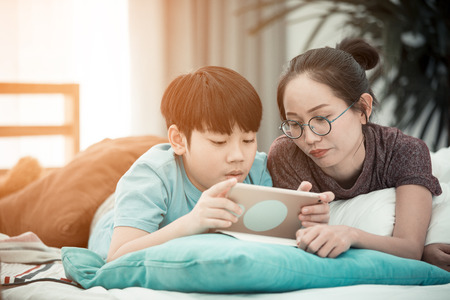 Asian boy with mother playing and learning tablet computer at home の写真素材