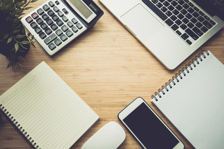 Mix of office supplies and gadgets on a wooden desk background. View from above.