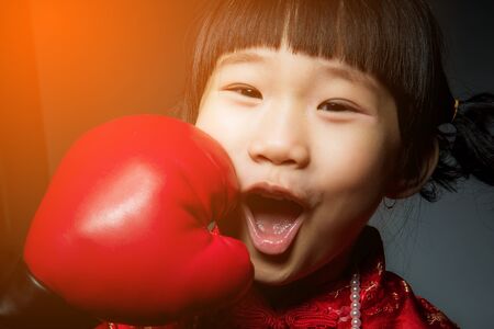 Happy chinese girl getting a hard punch from boxing glove fist.の写真素材