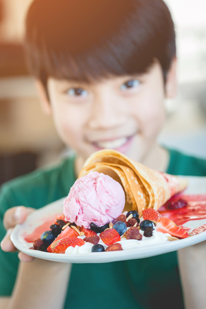 Excited asian child with smile face showing dessert. Focusing waffle on plate.の写真素材