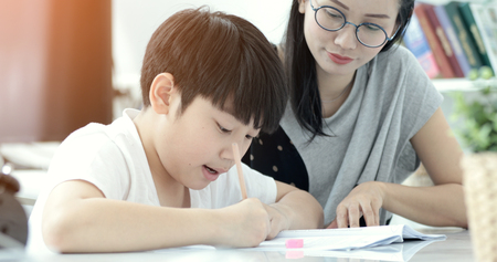 Serious Asian mother with son doing homework in the living room. Mom teaches son how to genius.の写真素材