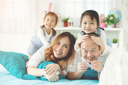 Happy asian family father mother and her daughter relexing on the bed at home ,with smile face.の写真素材