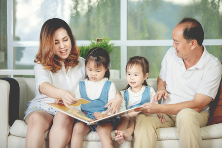 Portrait of asian father mother reading a cartoon book to her daughter at home.の写真素材